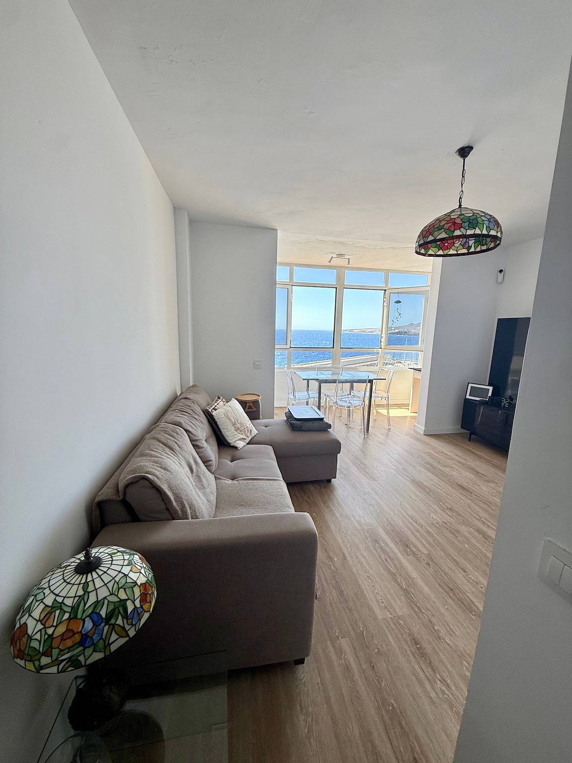 Living room with a grey corner sofa, looking towards the window and the sea