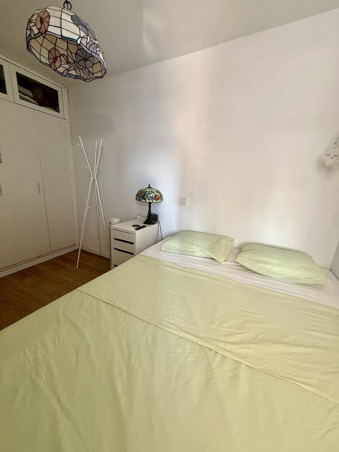 Double bed with light green linen and a stained-glass bedside lamp